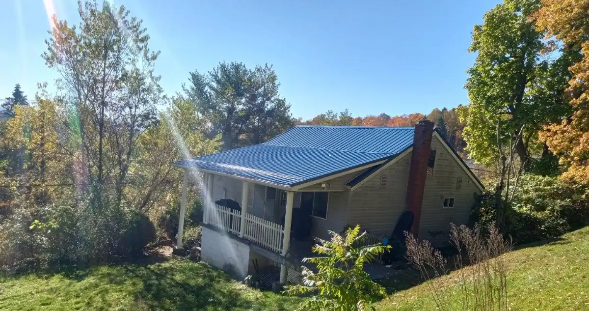 Pennsylvania home with a blue metal roof surrounded by trees in bright autumn sunlight.