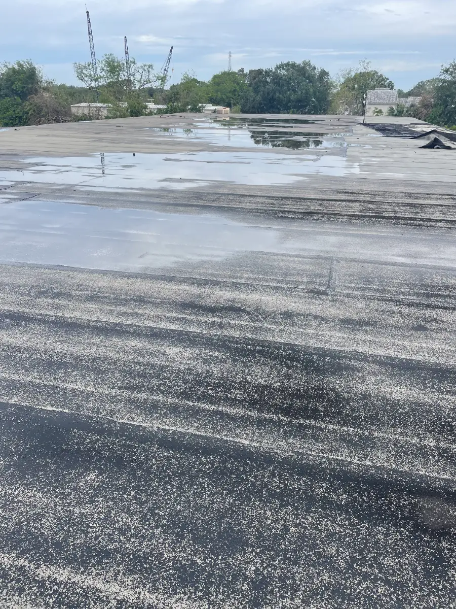 commercial-roof-ponding-water-after-winter Ponding water on a flat commercial roof showing drainage issues and surface wear after winter weather conditions