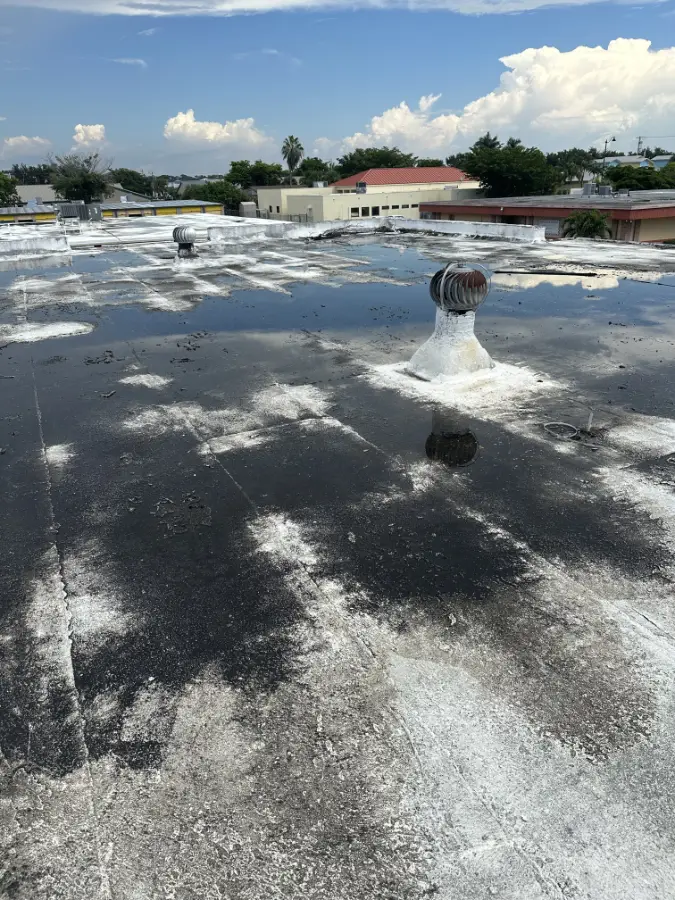 commercial-roof-ponding-water-worn-coating Ponding water on a commercial flat roof with worn coating, showing signs of deterioration and drainage issues