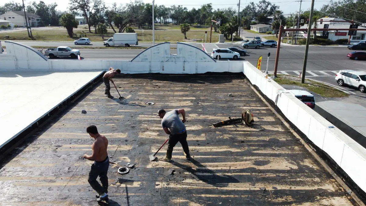 commercial-roof-repair-crew-removing-damaged-flat-roof Three workers removing damaged material from a commercial flat roof before repair and restoration work.