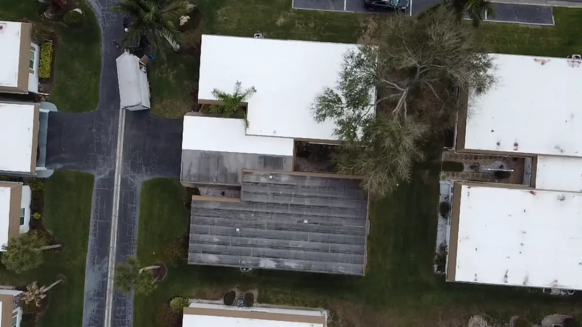 tpo-vs-epdm-flat-roof-comparison Aerial view of adjoining buildings with white single-ply roofs beside an older dark flat roof, illustrating different commercial flat roofing systems.